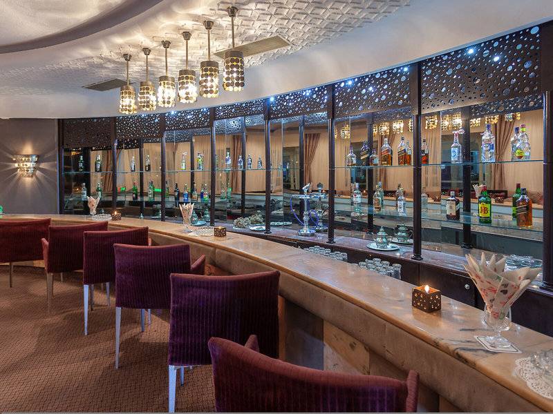 Innenansicht der Bar im Djerba Holiday Beach Hotel mit Bartheken, roten Stühlen und alkoholischen Getränken.