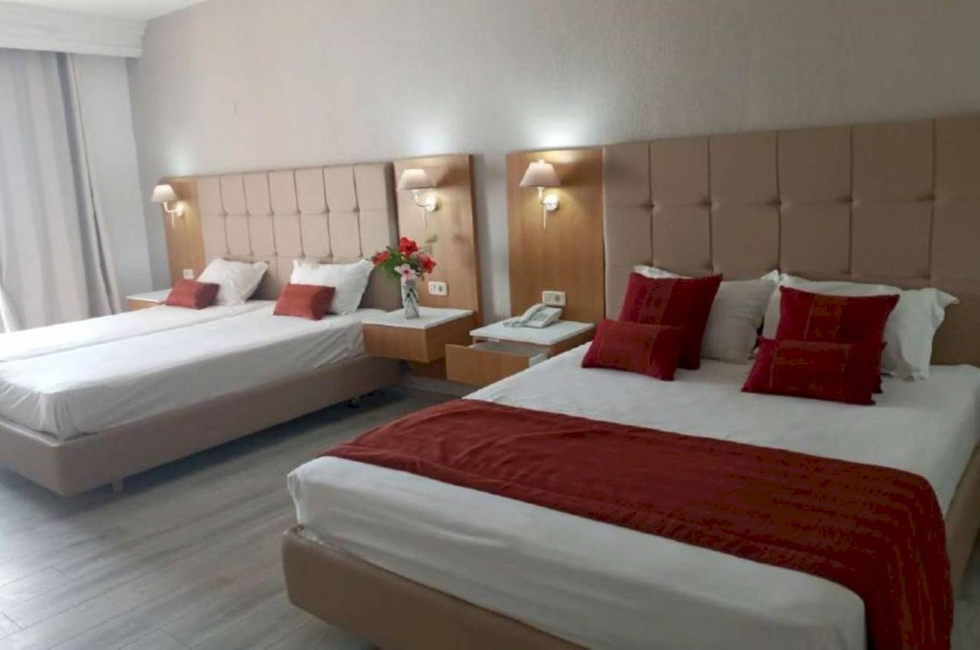 Zwei Doppelbetten in einem Hotelzimmer im Djerba Holiday Beach Hotel, jedes mit roten Kopfkissen und weißen Laken.
