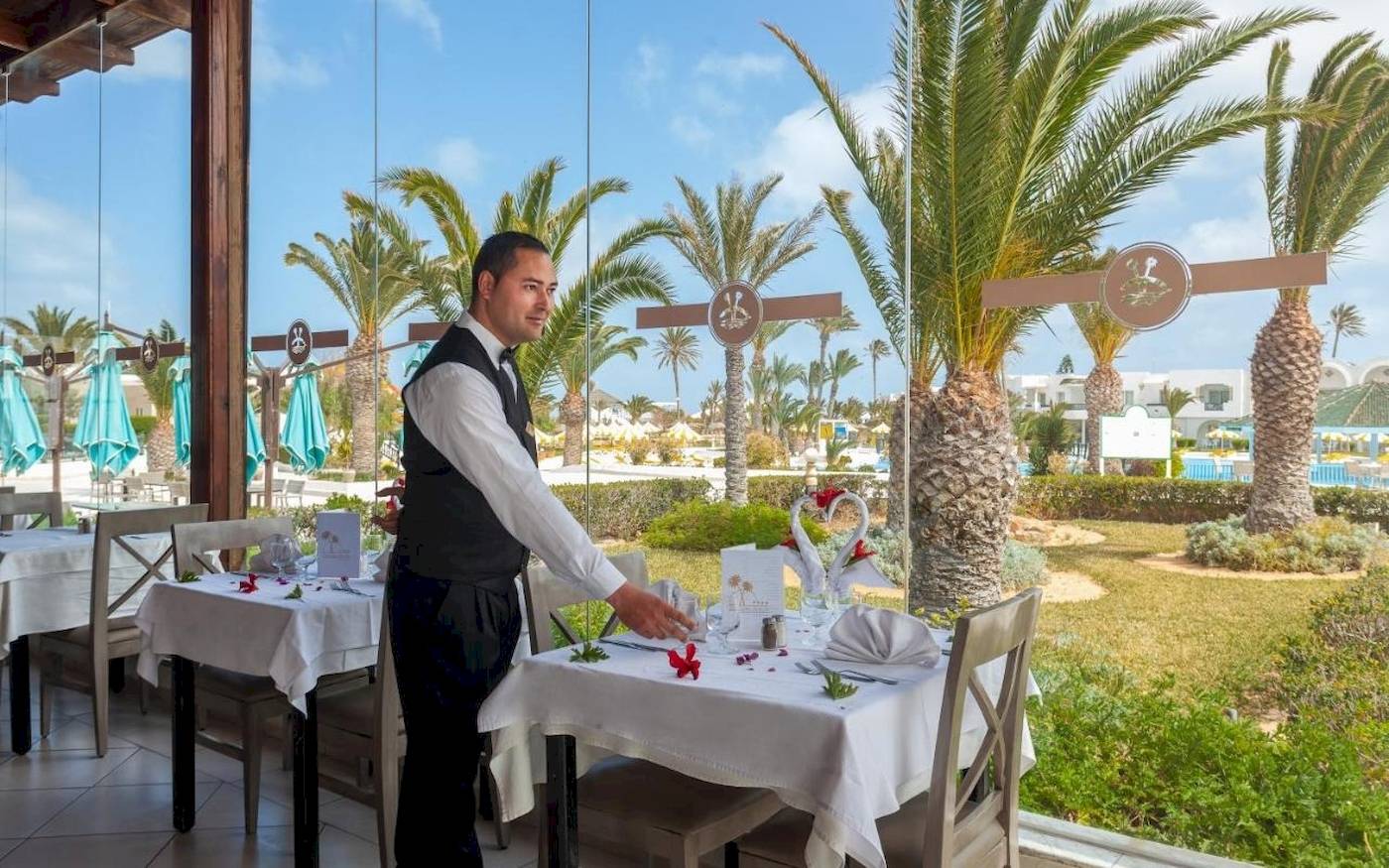Ein Kellner serviert einen Tisch im Freien im Djerba Holiday Beach Hotel.