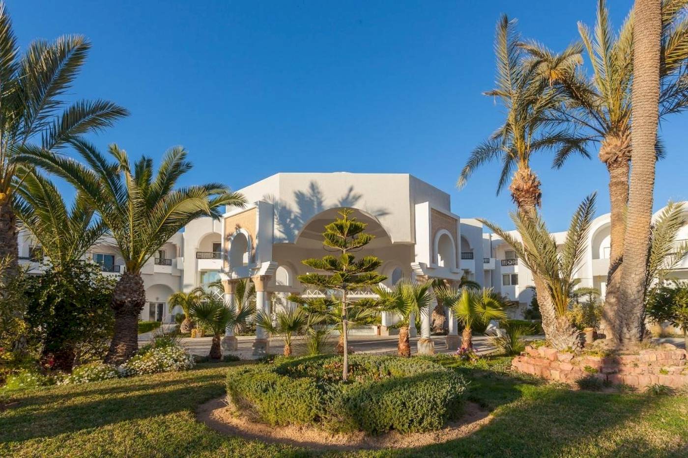Vorne des Djerba Holiday Beach Hotels mit Palmen und Gebäuden im Hintergrund