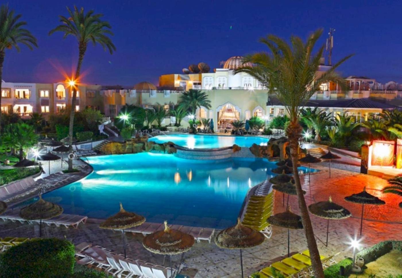 Abendliche Ansicht des Djerba Holiday Beach Hotels mit Swimmingpool und Palmen.