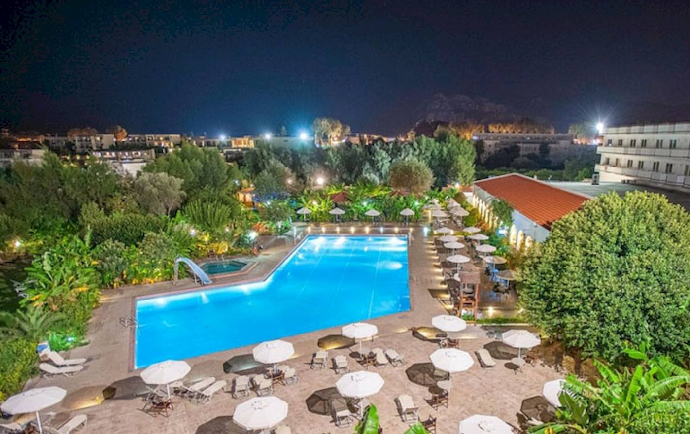 Nachtansicht des Irene Palace Beach Resorts mit Swimmingpool, Sonnenliegen und Schirmen.