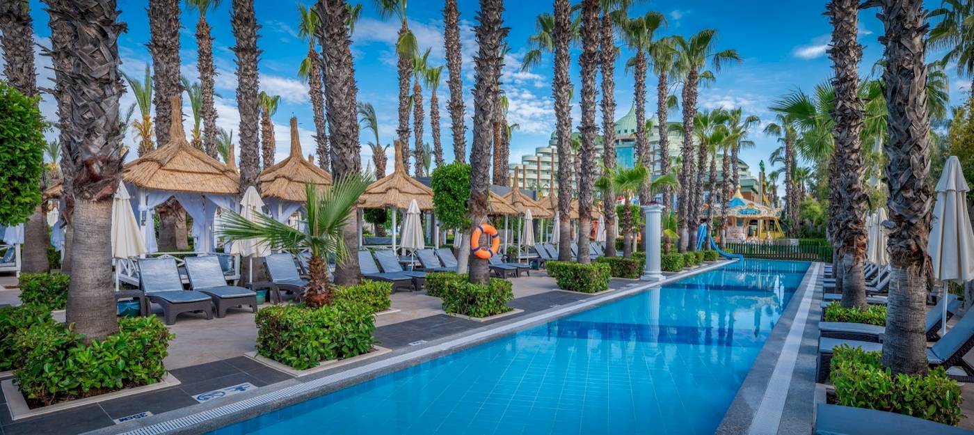 Außenbereich des Delphin Palace Hotels mit Swimmingpool, Liegestühlen und Palmen.