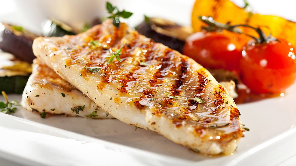 Zwei Stücke gebratener Fisch auf einem weißen Teller mit Gewürzen und Gemüse.