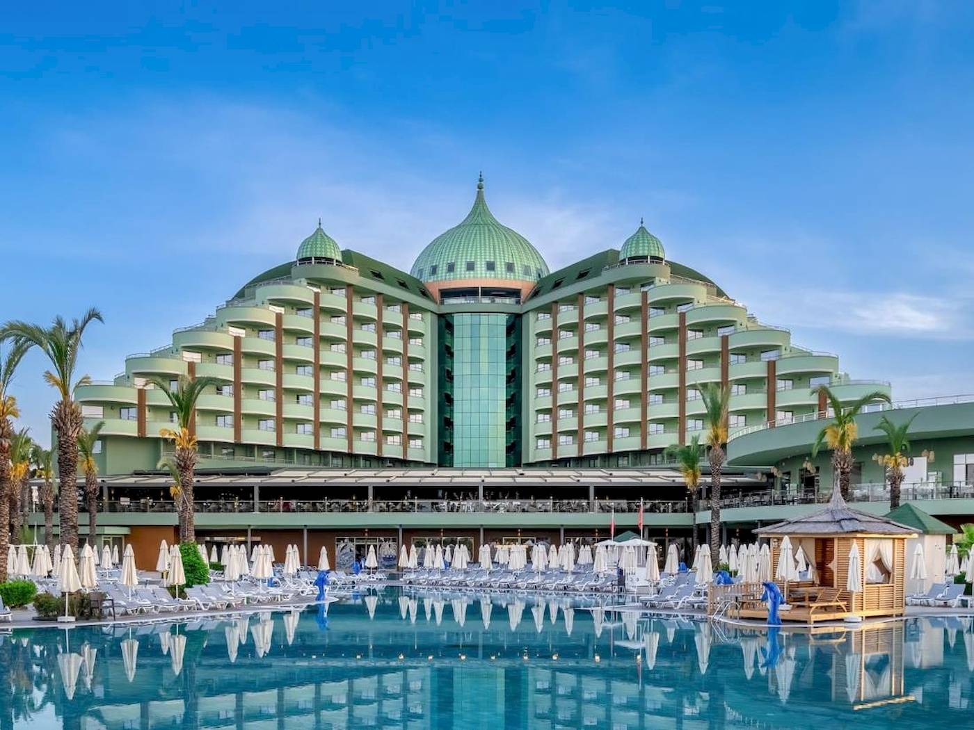 Außenansicht des Delphin Palace Hotels mit großen grünen Kuppeln, Swimmingpool und vielen Liegestühlen.