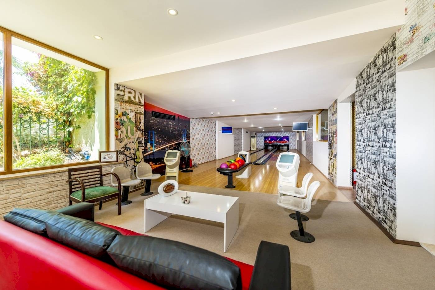 Bowlinghalle im VONRESORT Golden Coast mit Bowlingbahnen, Sitzmöbeln und einem Fenster mit Gartenblick.