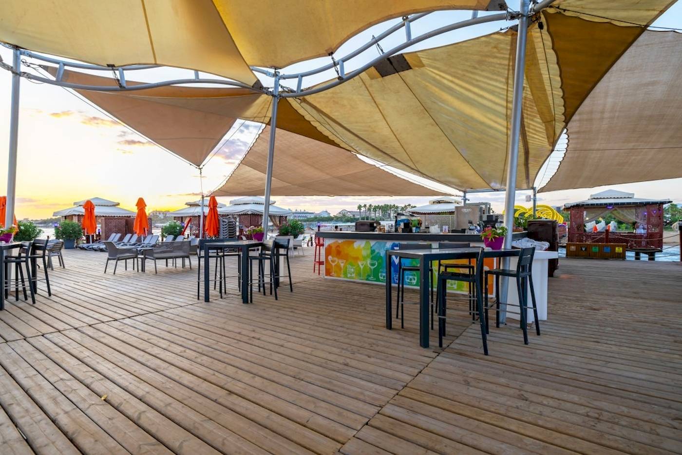 Terrasse des VONRESORT Golden Coast mit Tischen, Stühlen und Sonnenschirmen bei Sonnenuntergang.