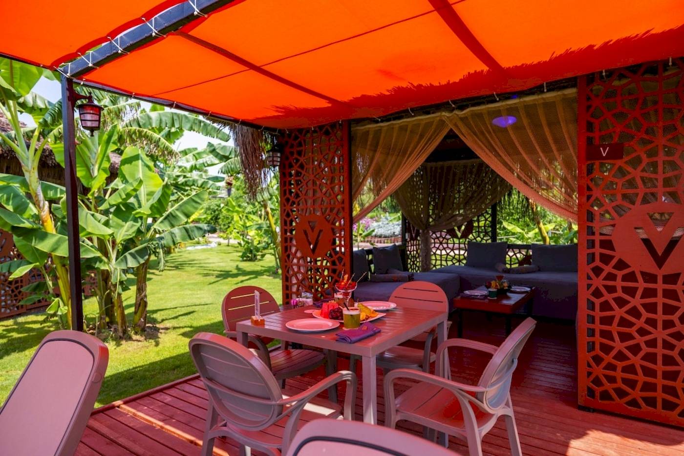 Sitzecke im Freien des VONRESORT Golden Coast mit rotem Sonnendach und grüner Wiese.