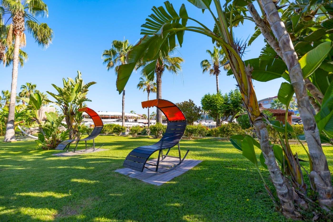 Zwei orange-schwarze Liegestühle im Garten des VONRESORT Golden Coast, umgeben von Palmen und Pflanzen.