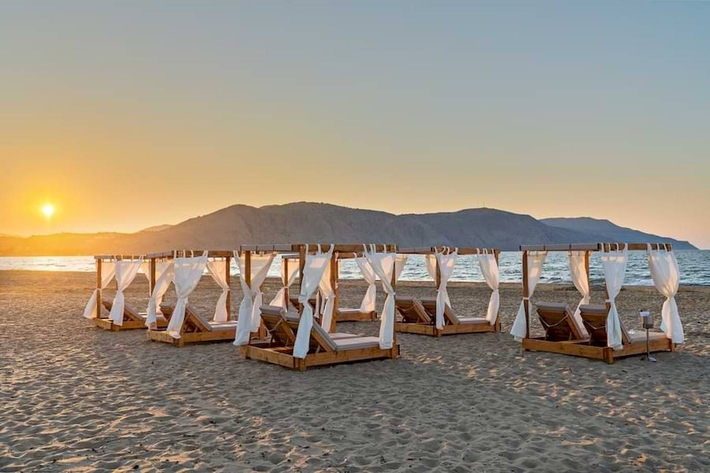 Georgioupolis Resort Aquapark & SPA mit Sonnenuntergang am Strand mit weißen Sonnenschirmen