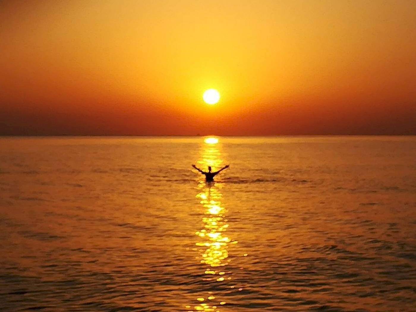 Eine Person schwimmt im Meer während des Sonnenuntergangs, mit der Sonne, die auf dem Horizont untergeht.