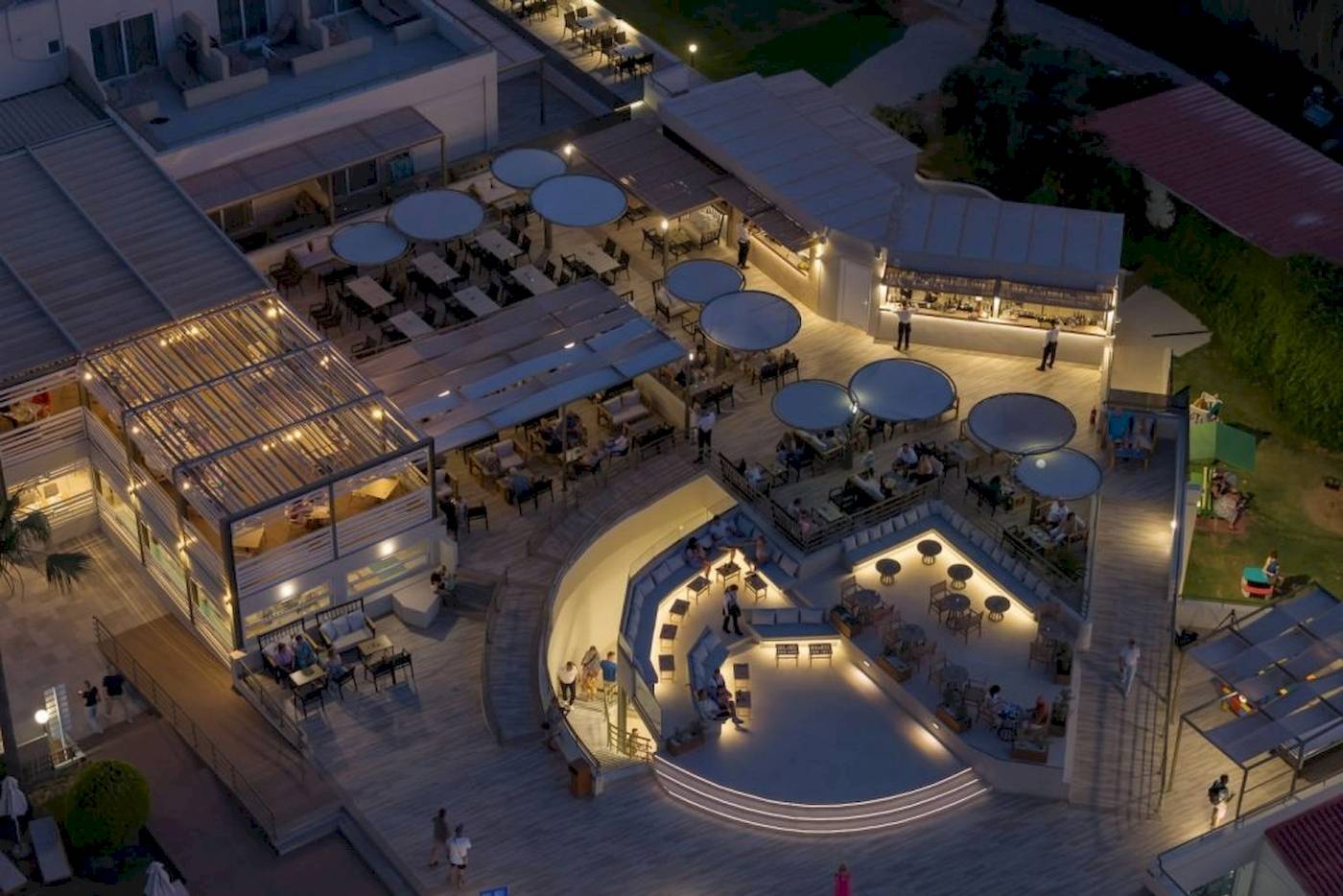 Abendluftaufnahme des Georgioupolis Resort Aquapark & SPA mit beleuchteten Terrassen und Gästen.