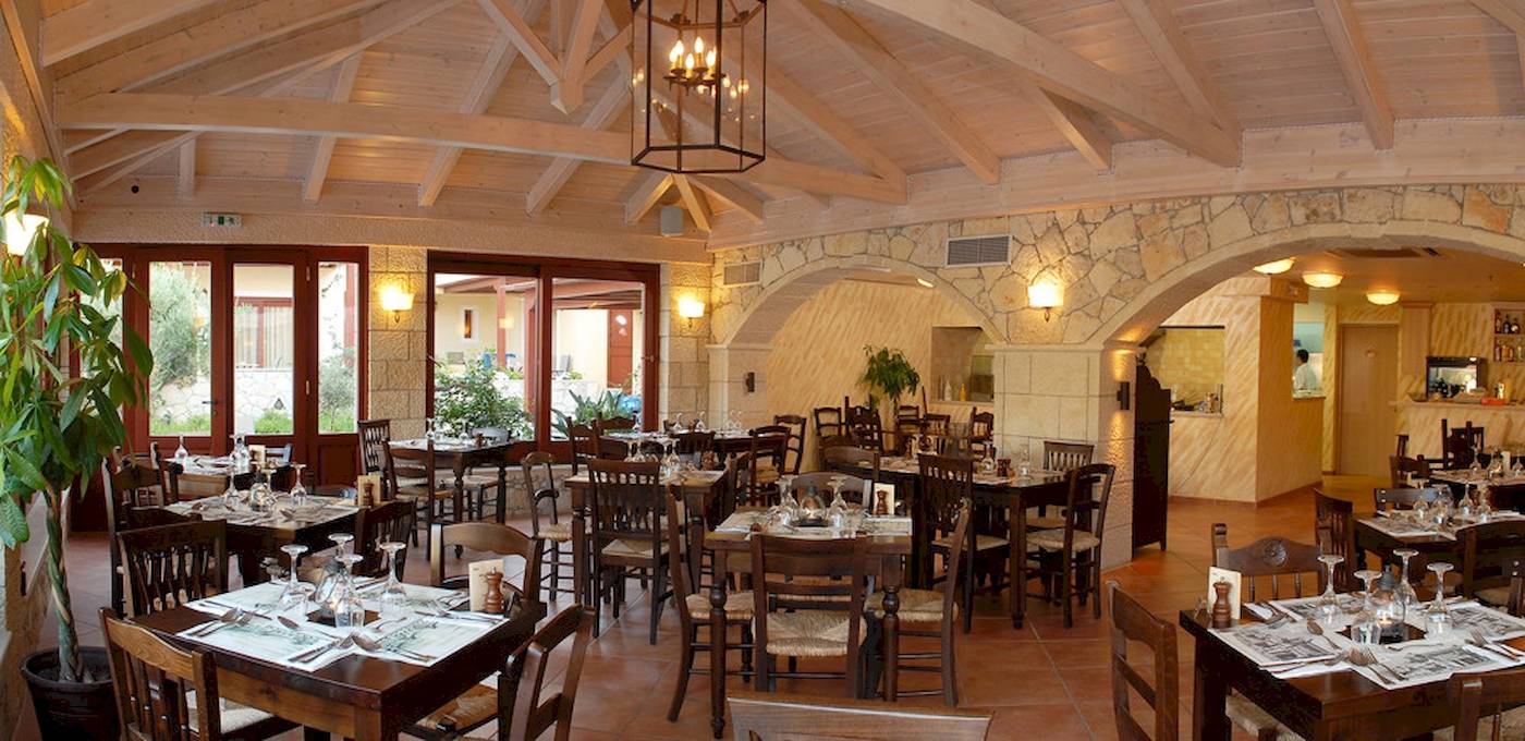 Innenansicht des Restaurants im Cactus Village Hotel mit Holztischen, Stühlen und einem hängenden Kronleuchter.