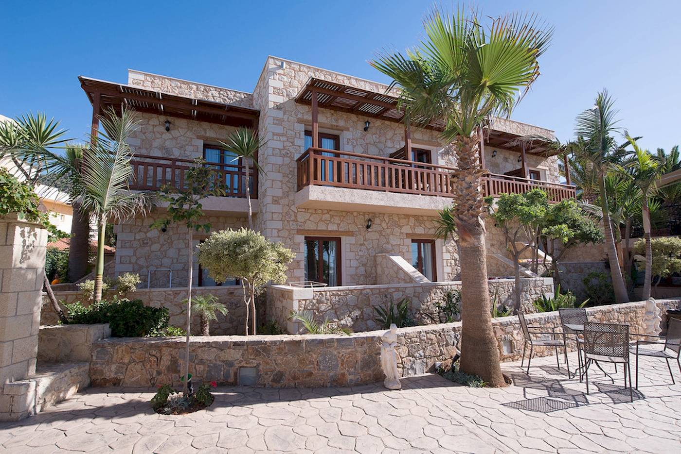 Außenansicht des Cactus Village Hotel & Bungalows mit Steinmauer und Palmen.