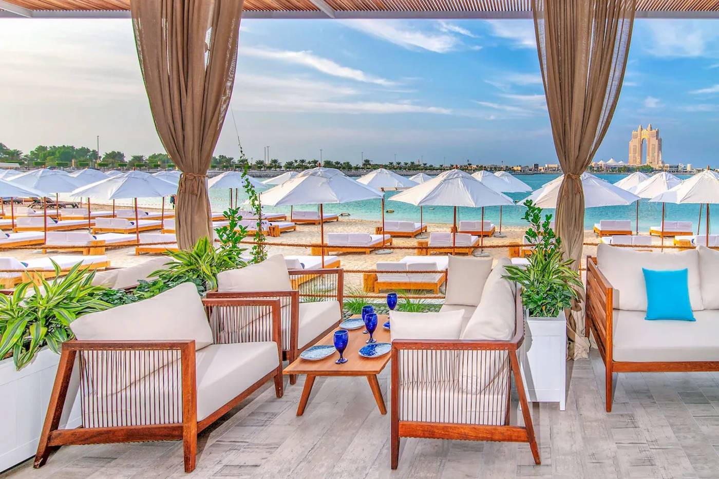 Außenbereich des Radisson Blu Hotel & Resort in Abu Dhabi mit weißen Sonnenschirmen und Möbeln am Strand.