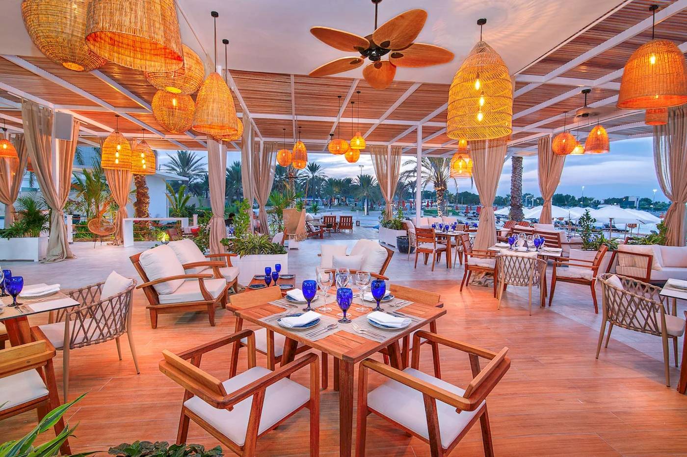 Innenbereich des Restaurants im Radisson Blu Hotel & Resort, Abu Dhabi Corniche, mit hängenden Lampen und gedeckten Tischen.