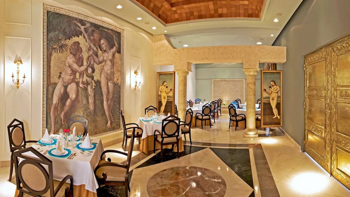 Speisesaal im Iberostar Grand Bavaro Hotel mit eleganten Tischen, Stühlen und Wandgemälden.