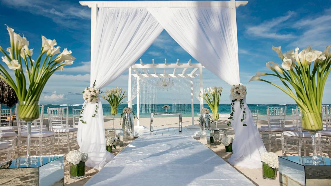 Strandhochzeitszeremonie im JOIA Bávaro by Iberostar mit weißen Vorhängen und Blumen.