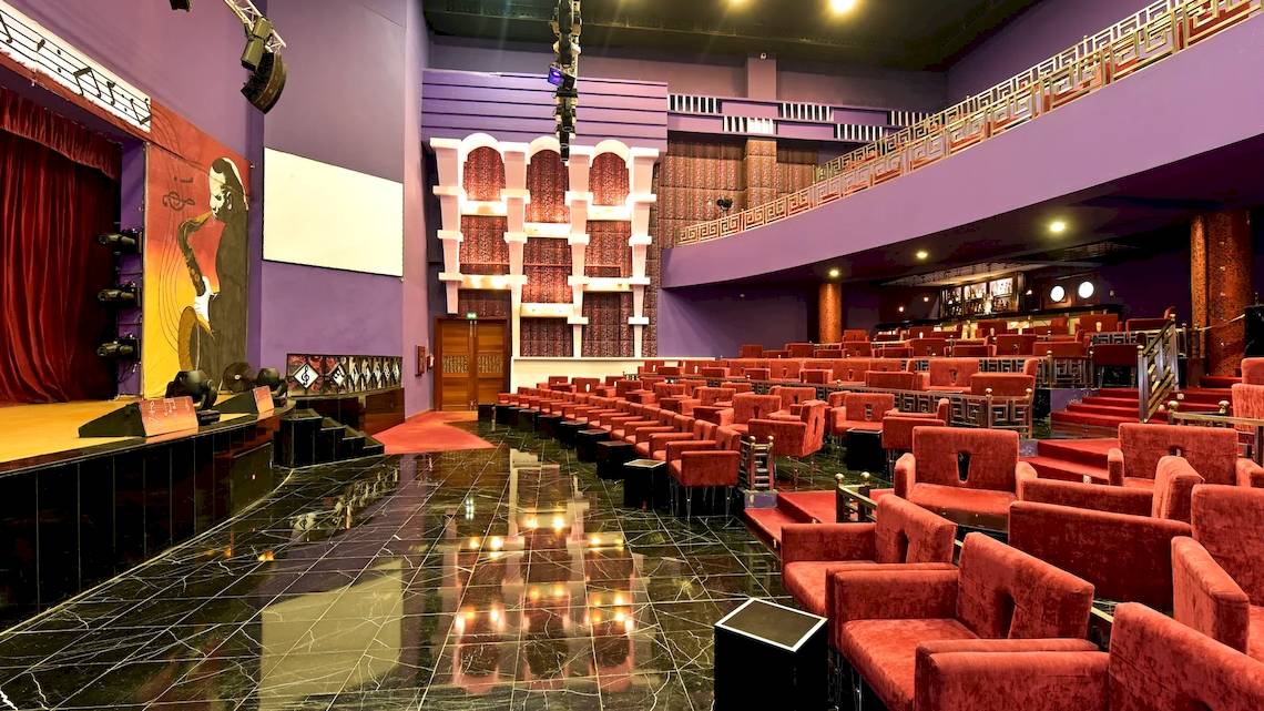 Ein Kinosaal mit leeren roten Stühlen, roter Teppich, und rote Vorhänge.