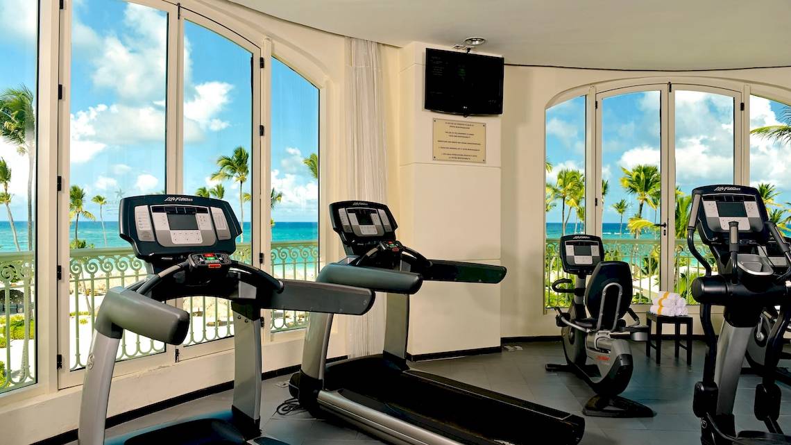 Fitnessraum im JOIA Bávaro by Iberostar Hotel mit Blick auf das Meer und Palmen.