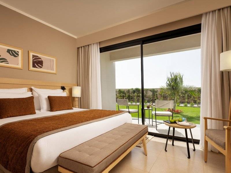 Hotelzimmer im Jaz Elite Amara mit großem Bett, Ausblick auf grüne Landschaft und Terrassenmöbel.
