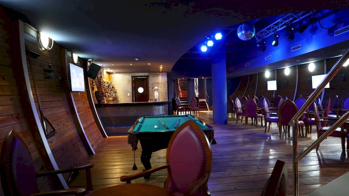 Pool-Lounge im JOIA Bávaro Hotel mit grünem Billardtisch und blauer Beleuchtung.