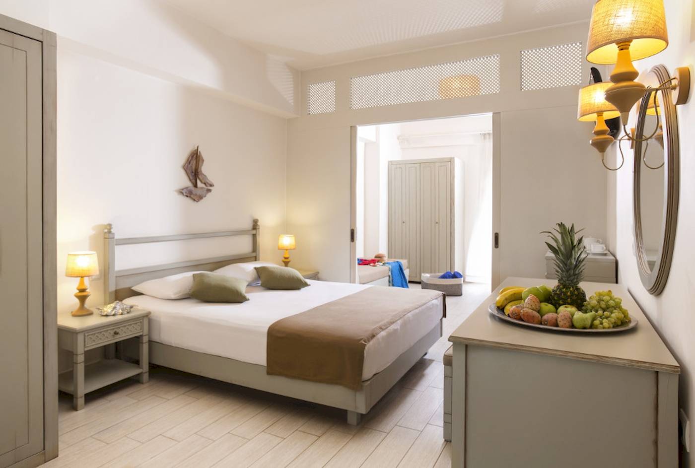 Innenansicht eines Zimmers im Almyrida Beach Hotel mit einem Bett, Nachttischen und Früchten auf einem Tisch.
