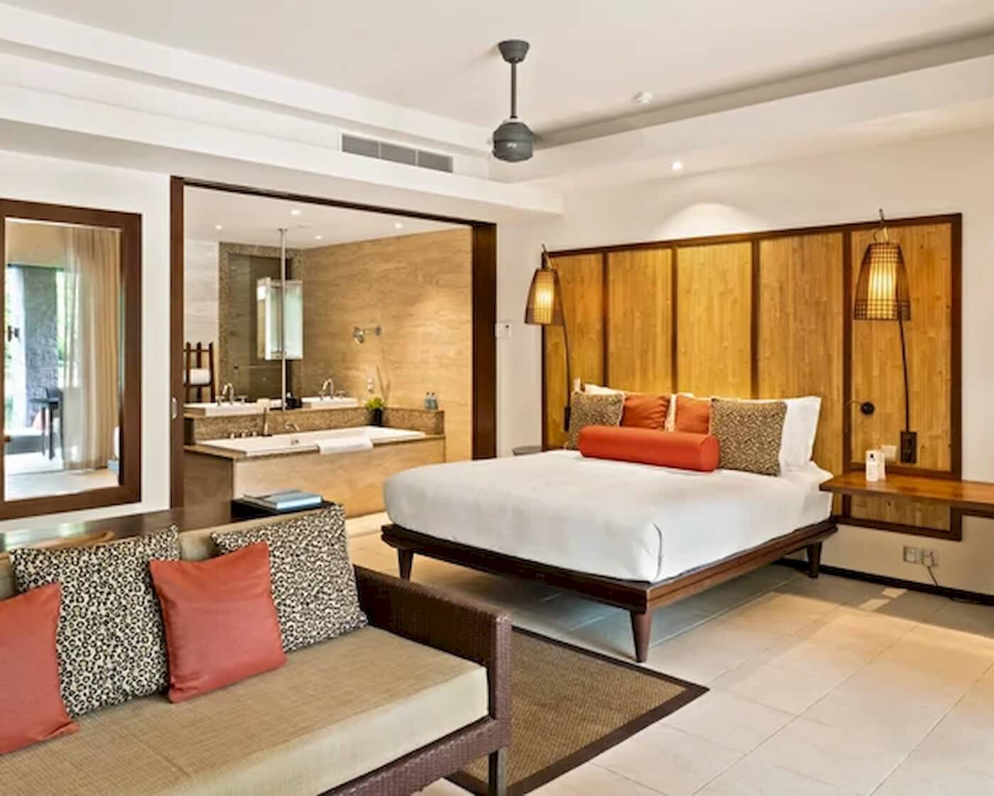 Innenansicht eines Schlafzimmers im Constance Ephelia Resort mit großem Bett, Sofa, Badewanne und Dekor.