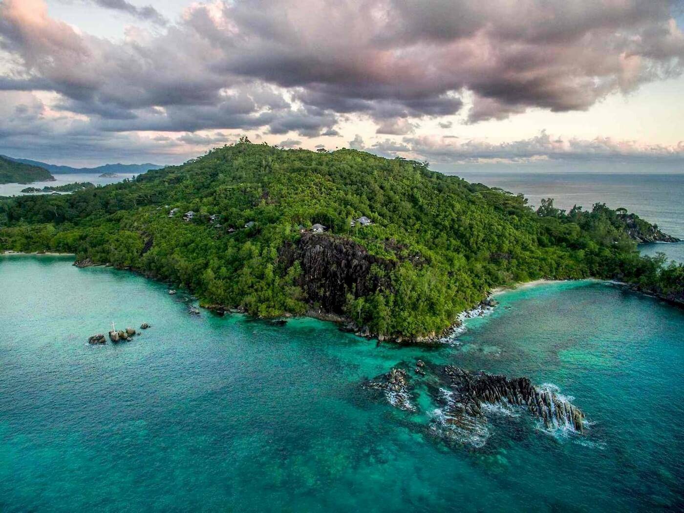 Aussicht auf das Constance Ephelia Resort auf einer kleinen Insel mit dichtem Grün und türkisfarbenem Wasser.