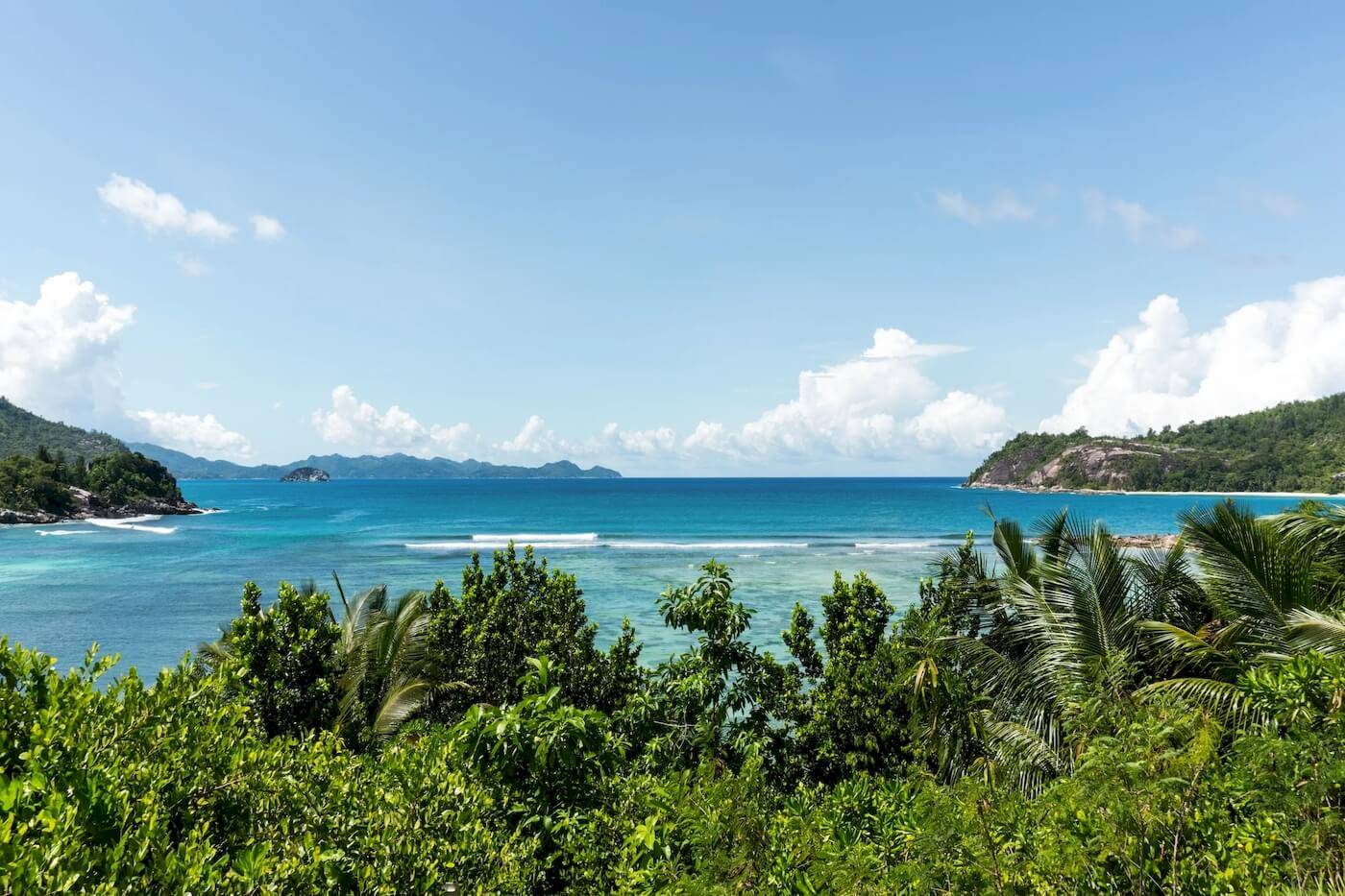 Aussicht auf das Meer vom Constance Ephelia Resort aus, mit blauem Himmel, Wellen und grünen Pflanzen.
