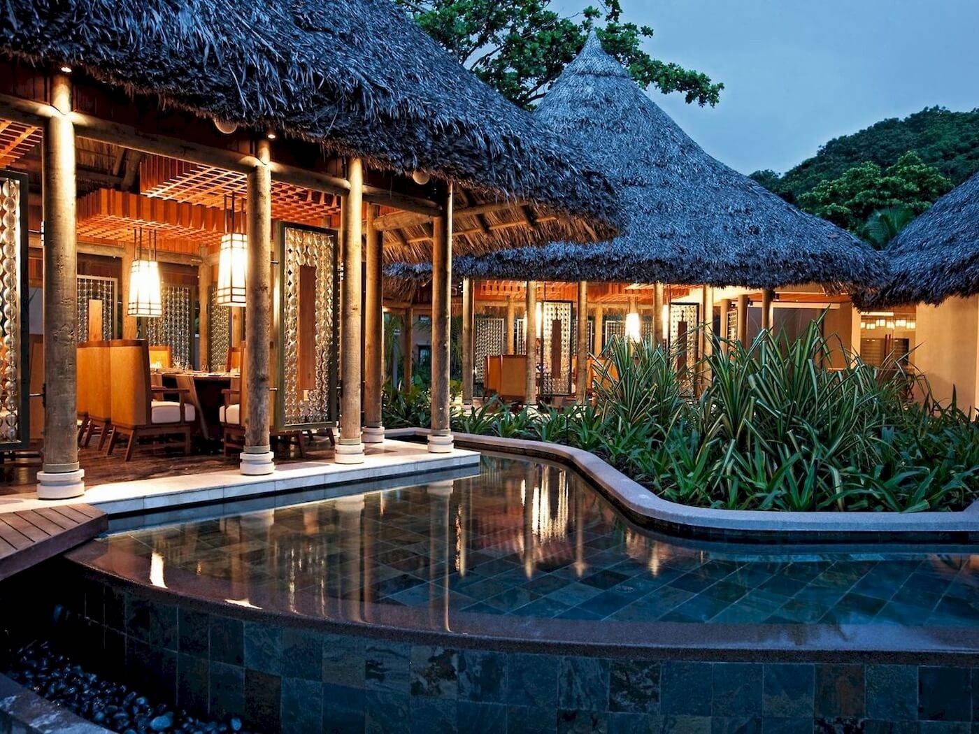 Außenbereich des Constance Ephelia Resorts mit Swimmingpool und traditionellen Strohdächern