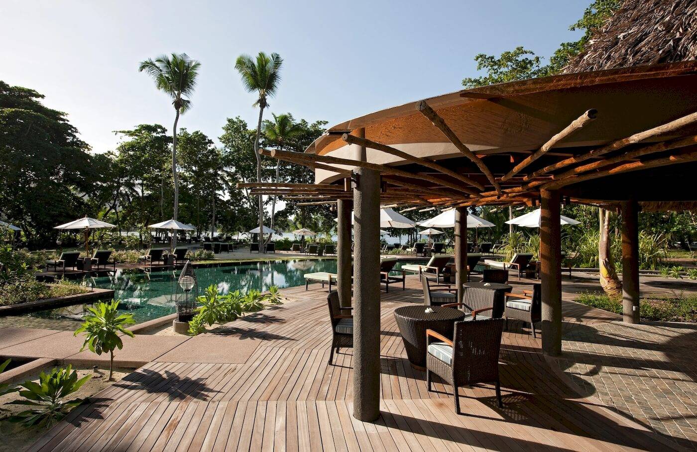 Terrasse im Constance Ephelia Resort mit Tischen, Stühlen und Sonnenschirmen am Swimmingpool.