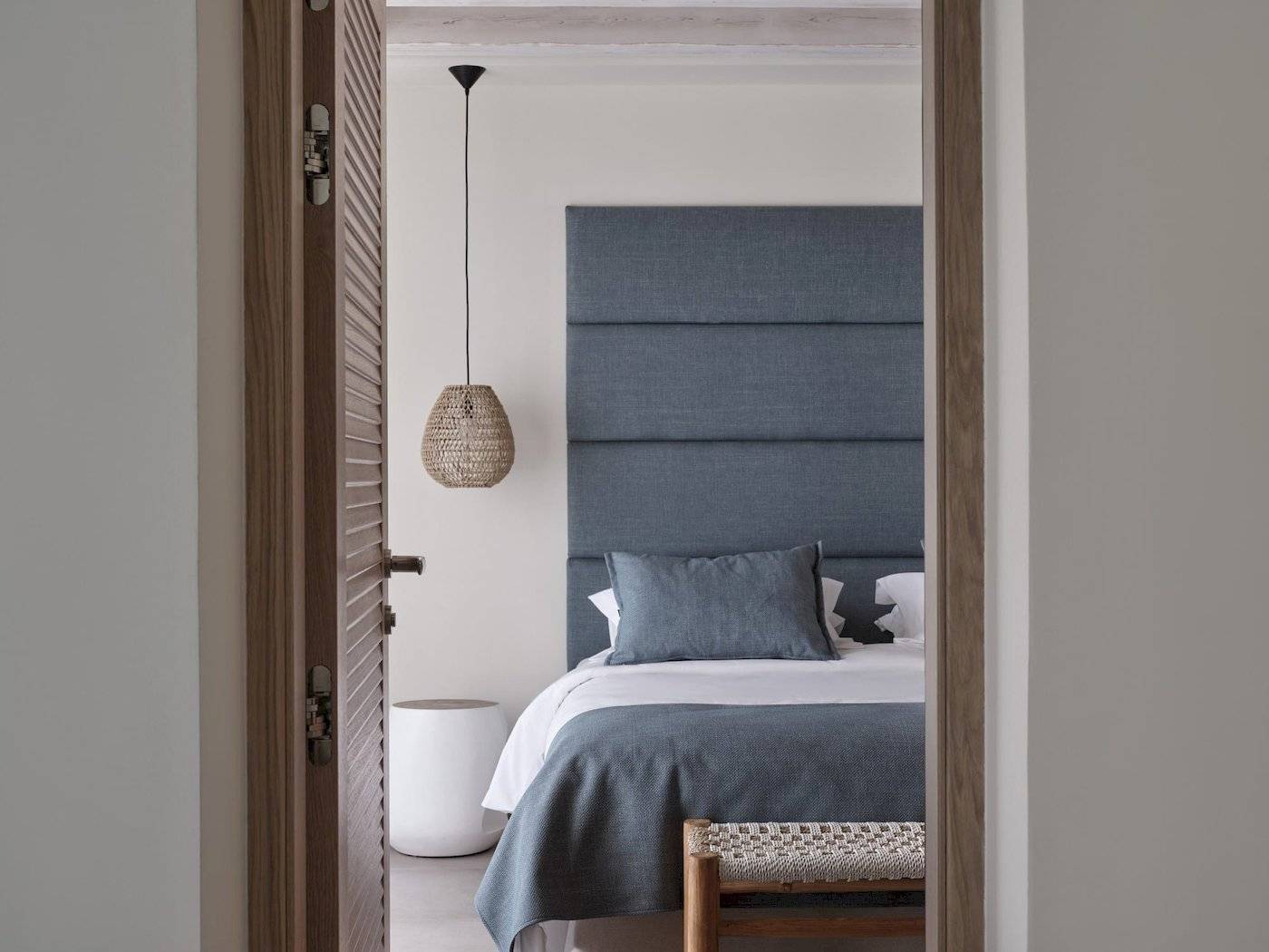 Zimmer im Atlantica Beach Resort Kos mit einem Bett, blauem Kopfteil und einem weißen Stuhl.