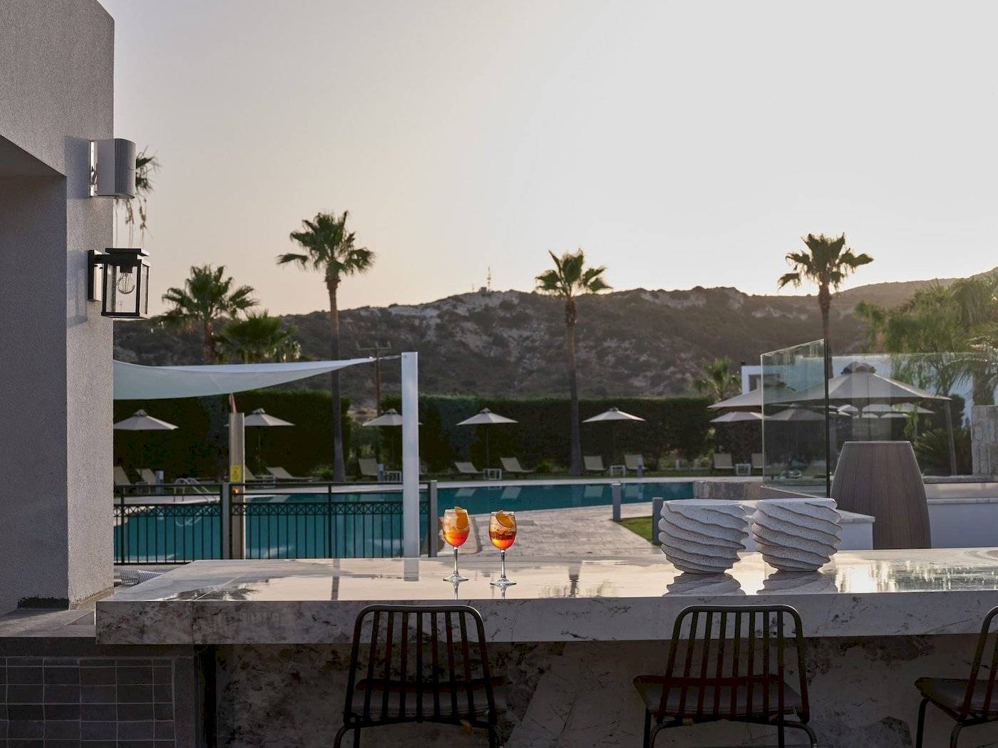 Abendlicher Blick auf den Pool des Atlantica Beach Resort Kos mit Cocktails und Palmen.