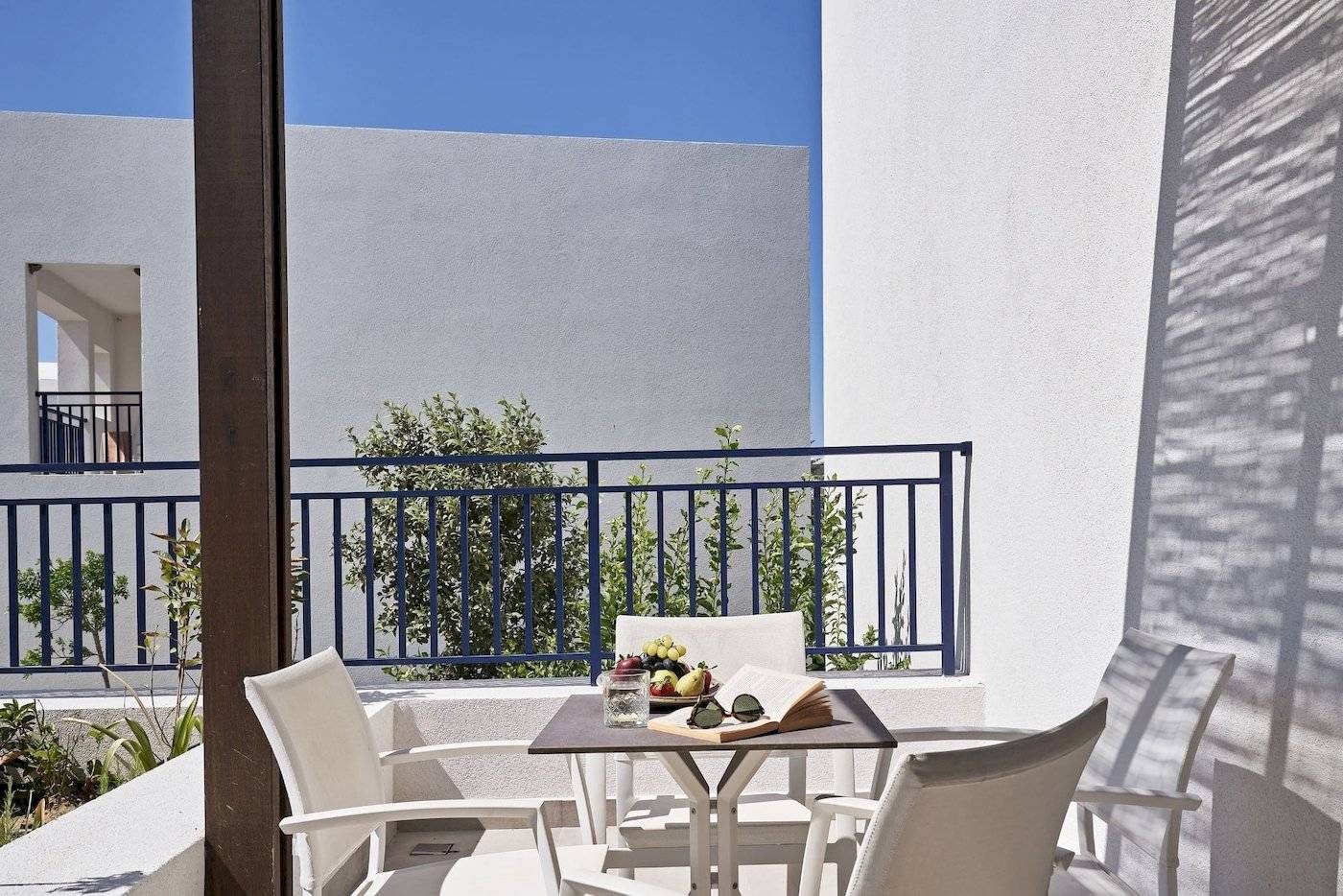 Balkon des Atlantica Beach Resort Kos mit Tisch und weißen Sesseln vor blauem Geländer.