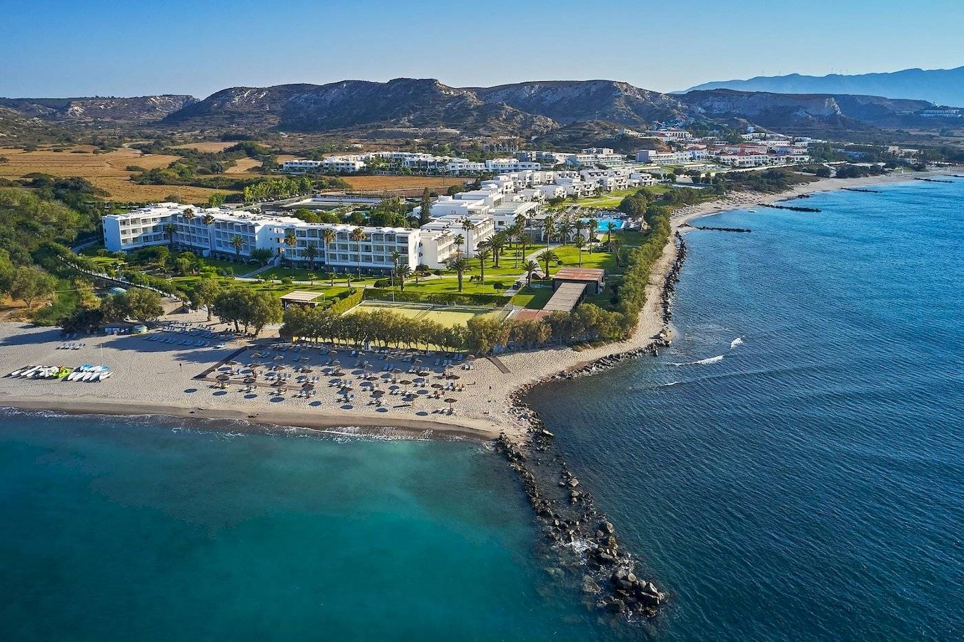 Gesamtansicht des Atlantica Beach Resort Kos am Strand mit vielen Liegestühlen und Hotelgebäuden.