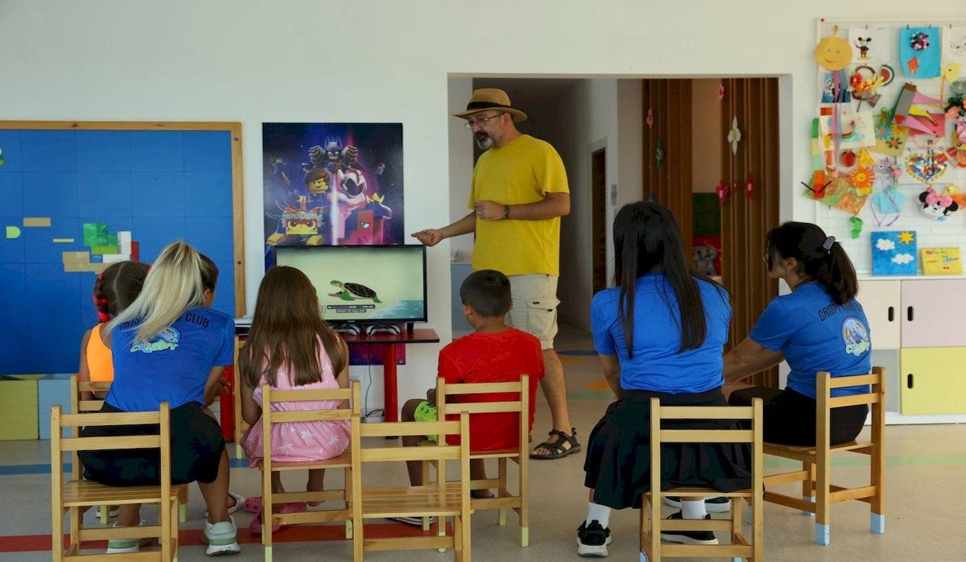 Hotelmitarbeiter zeigt Kindern einen Film auf dem Monitor im Klassenzimmer.