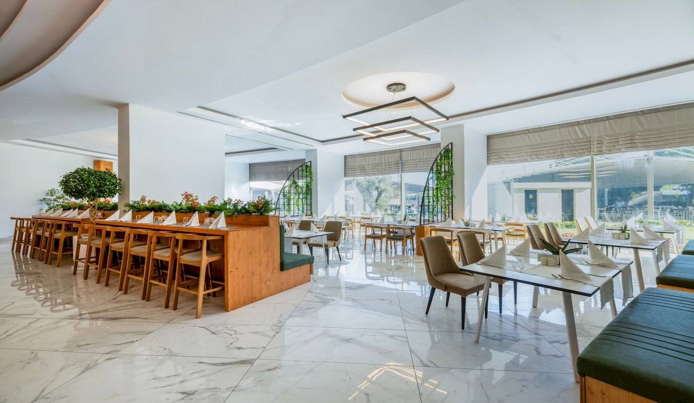 Ein modernes Restaurant mit weißen Wänden, Marmorböden und großen Fenstern im Nirvana Cosmopolitan Hotel.