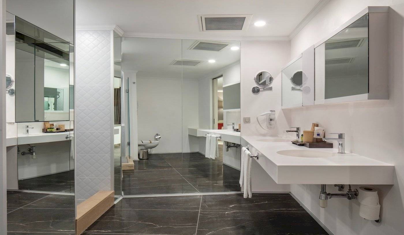 Das Badezimmer des Nirvana Cosmopolitan Hotels mit weißen Waschbecken und schwarzen Marmorboden.