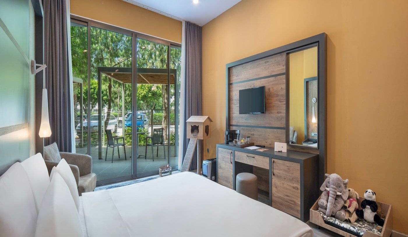 Ein Hotelzimmer im Nirvana Cosmopolitan mit Panoramafenstern, die auf einen Garten und eine Terrasse mit Tischen und Stühlen hinausführen.