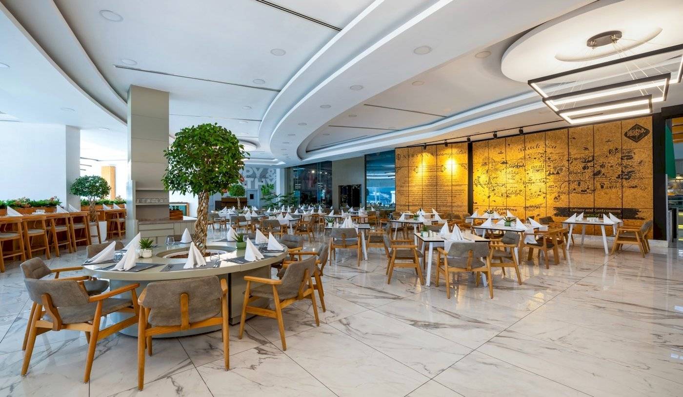 Innenbereich des Nirvana Cosmopolitan Hotels mit gerundeten Tischen, Holzstühlen und weißer Marmorfliesen.