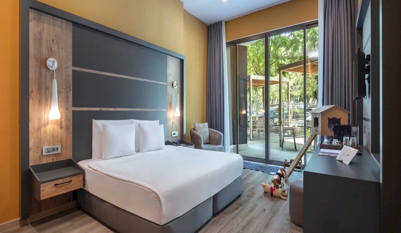 Innenansicht eines Hotelzimmers des Nirvana Cosmopolitan Hotels mit Bett, Nachttischen und offenem Balkon.