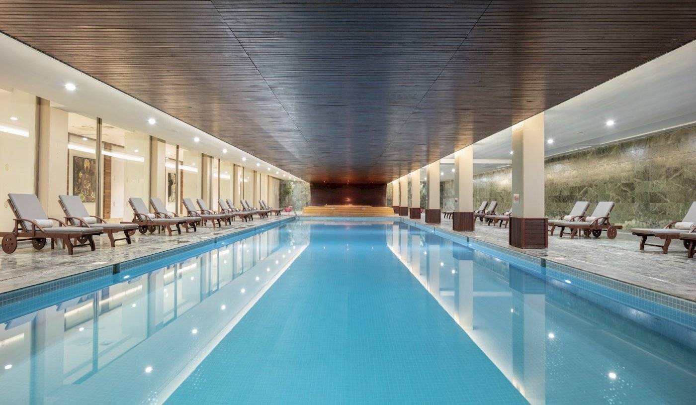 Innenpool des Nirvana Cosmopolitan Hotels mit Liegen und beleuchteten Wänden.