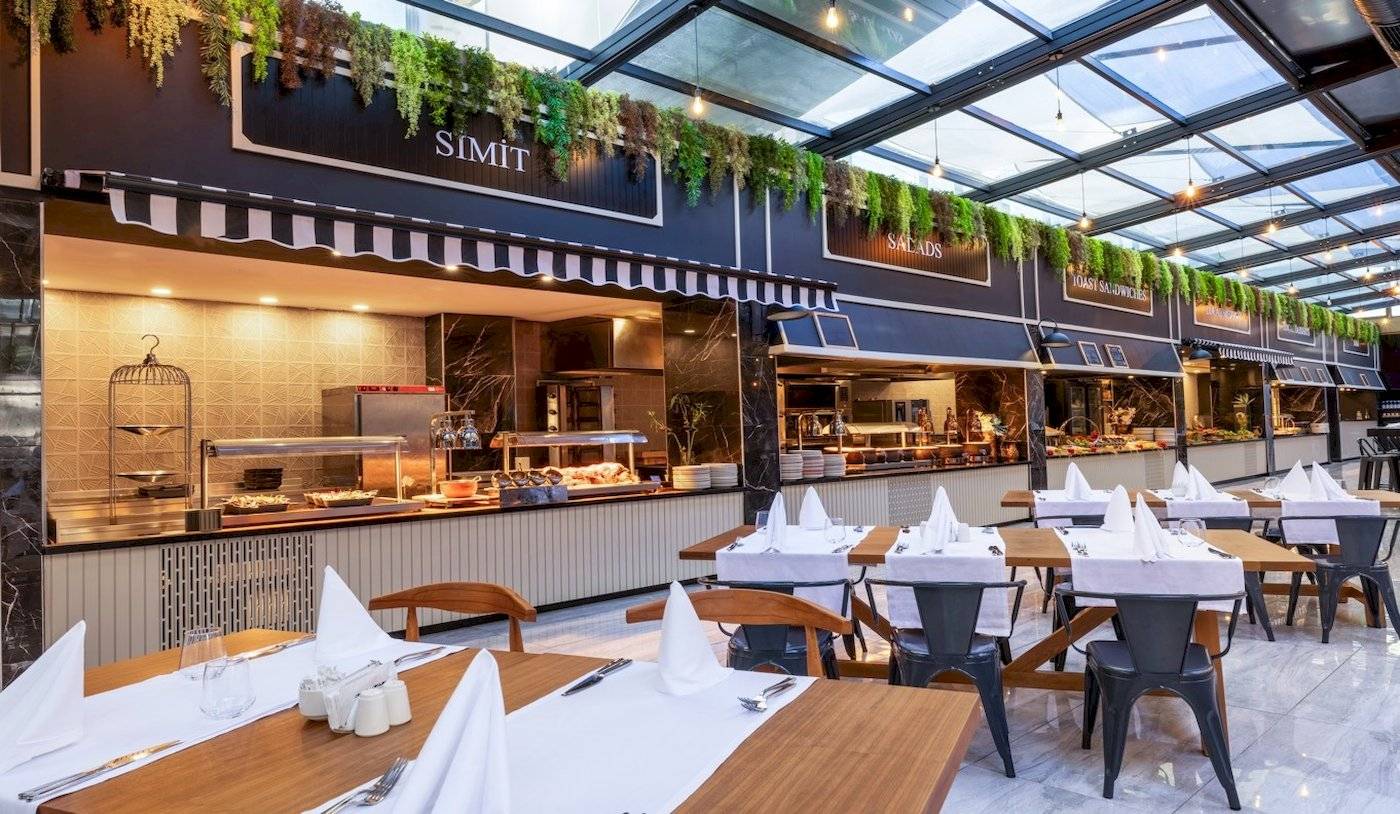 Speisebereich des Nirvana Cosmopolitan Hotels mit Tischen, Stühlen und Pflanzendekoration.