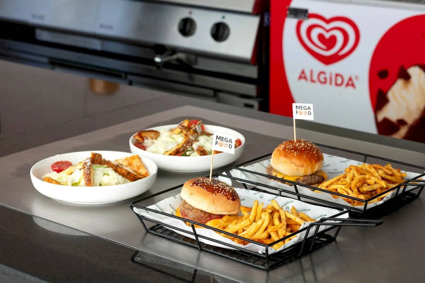 Drei Gerichte von Megasaray Resort Side: Burger, Pommes und Salat, serviert auf einer Theke.