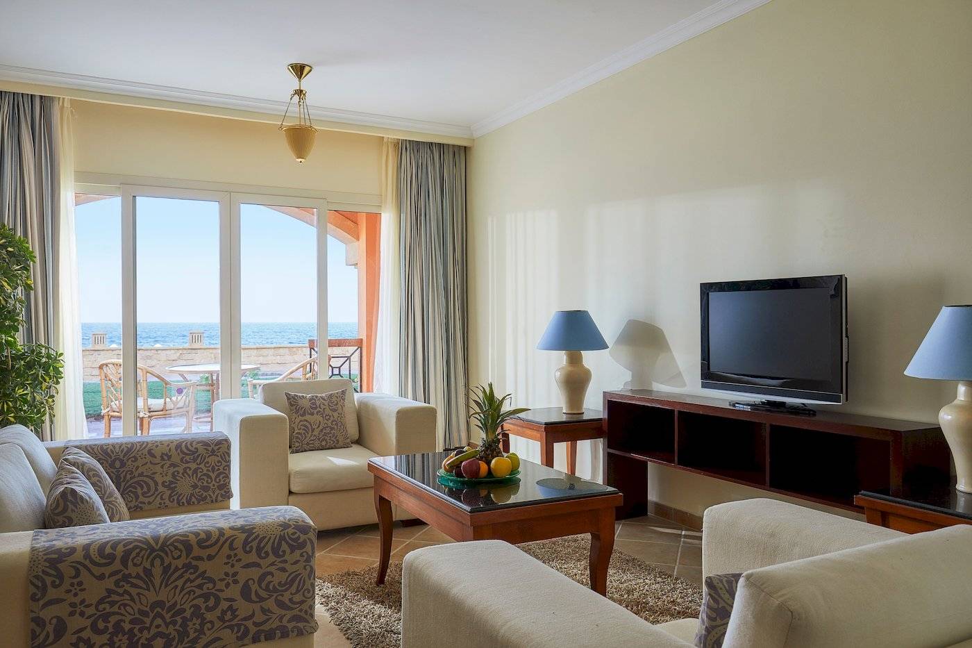 Wohnzimmer im Jaz Grand Marsa Hotel mit Meerblick, Fernseher, Sofas und Tisch mit Früchten.