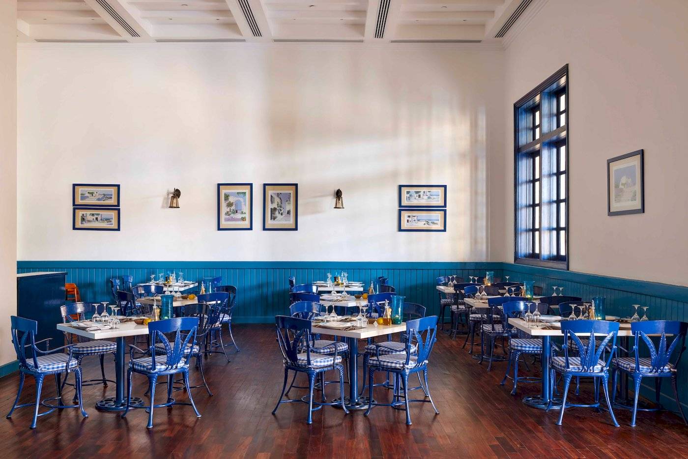 Innenraum des Jaz Grand Marsa Restaurants mit blauen Stühlen und Tischen, weißen Wänden und Holzboden.