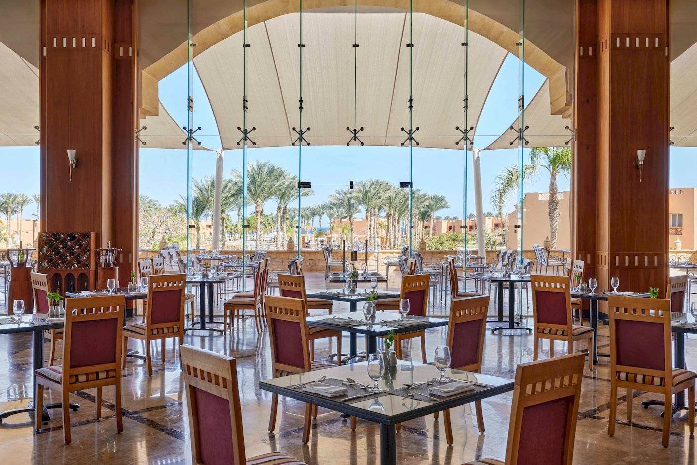 Restaurantbereich im Jaz Grand Marsa Hotel mit Glaswänden und Blick auf Palmen.