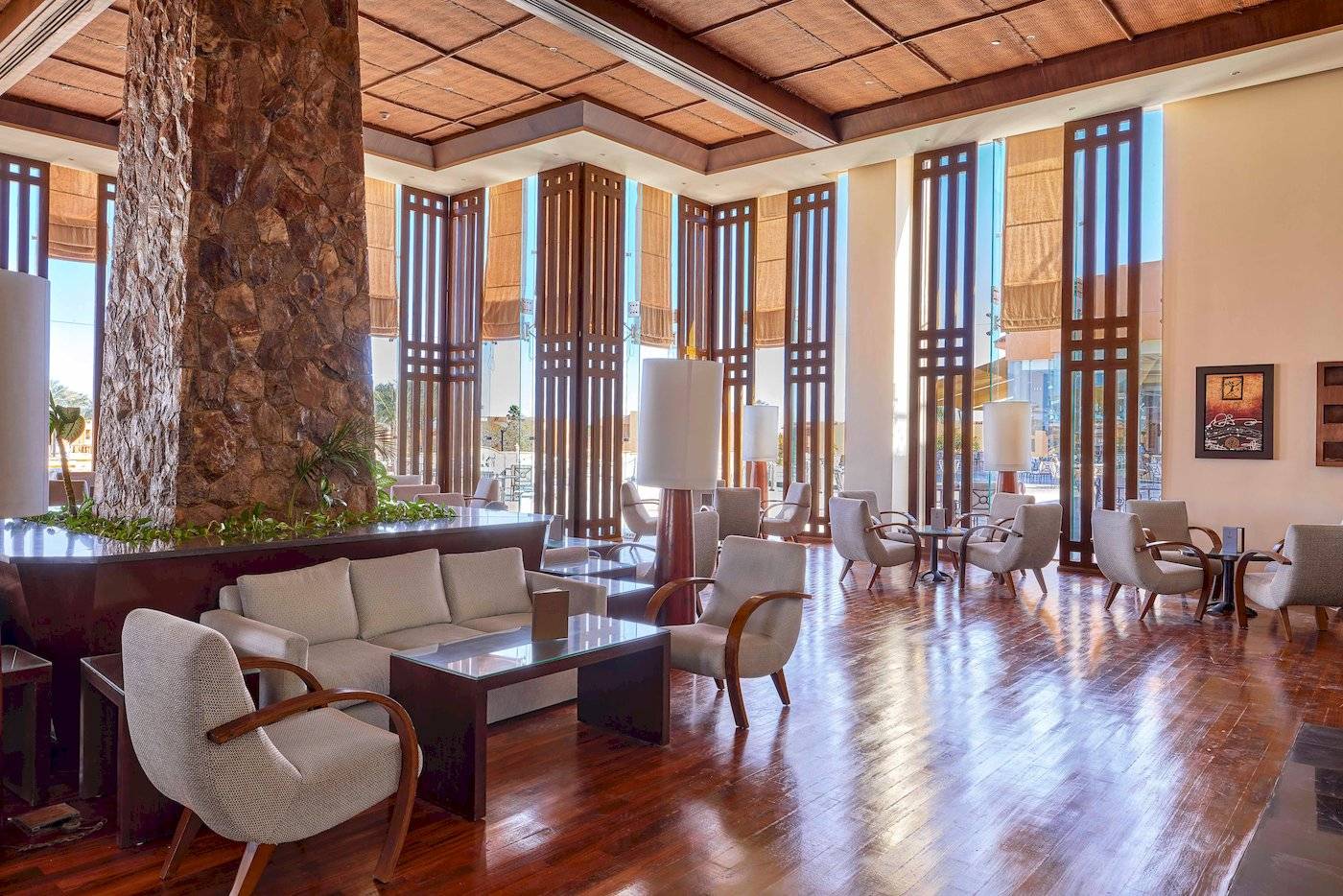 Innenansicht der Lobby des Jaz Grand Marsa Hotels mit Holzboden, Möbeln und einer zentralen Säule.