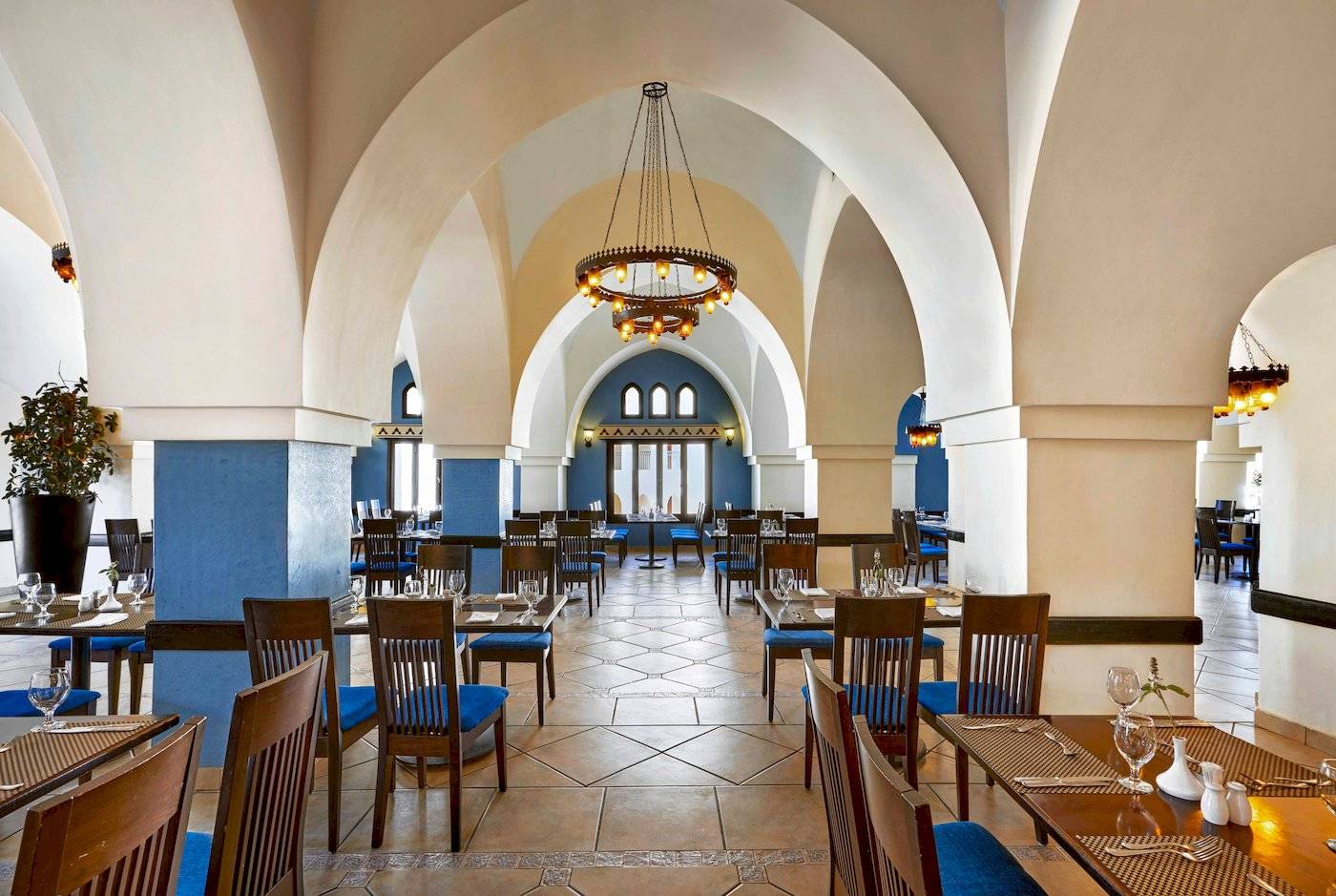 Innenbereich des Restaurants im Jaz Lamaya Resort mit blauen Säulen und Holztischen.
